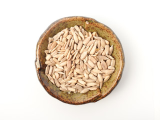 Top view of natural shelled organic sunflower seeds on pottery plate isolated on white background. It often eaten as a snack.  The seeds contain vitamin E. Food and snack concept. With copy space.