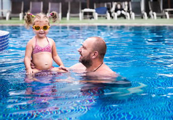 Fototapeta premium Dad teaches a little daughter to swim in the pool.