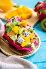 Mix tropical fruits salad served in half a dragon fruit on wooden table