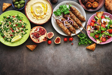 Assorted Middle Eastern and arabic dishes on a dark rustic background. Hummus,tabbouleh, salad Fattoush,pita,meat kebab,falafel,baklava,pomegranate. Halal food.Top view, flat lay, copy space - obrazy, fototapety, plakaty