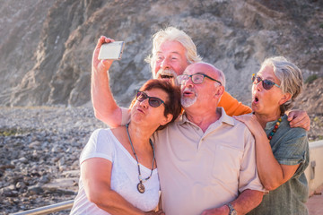 group of seniors and mature people taking a selfie together at the beach with the rocks on the backround -- having fun together at the sunet