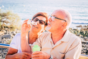 couple of seniors married sit on the beach blowing a bubble of soap with the sea in the background