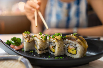 A woman eating sushi roll Mackerel or saba with chopstick in Black plate ,Japanese Food Style
