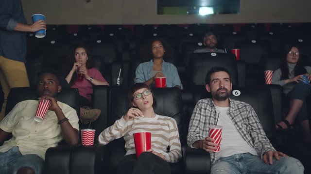Young man is coming to cinema late holding food and drink disturbing people while spectators are watching video. Culture, time and entertainment concept.