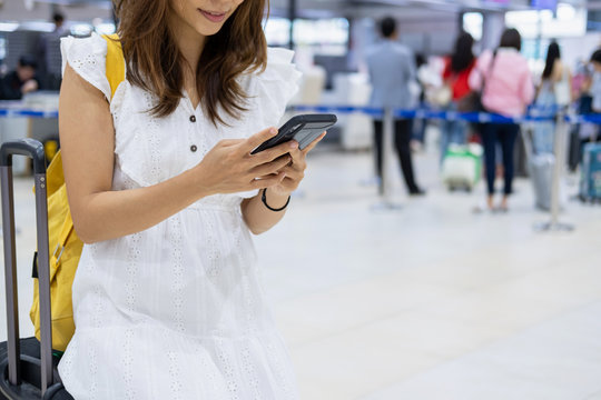 Young woman traveler using her smartphone to check flight in the airport
