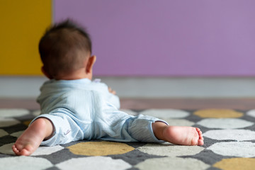 Portrait of young asian baby toddler laying on floor on carpet with colorful background. Back of...