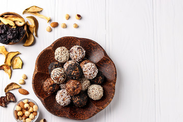 Energy balls of nuts, oatmeal and dried fruits with flax and sesame seeds, coconut flakes on a wooden plate of coconut on a white background, horizontal orientation