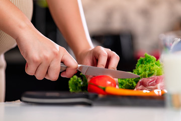 Young asian pregnant woman in ketchen. Cutting tomato with large knief. Close up of hand. Parenthood concept.
