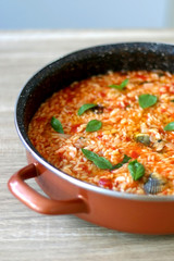 Orzo pasta, cooked with tomato sauce, vegetables and seafood, served on a table. Selective focus.