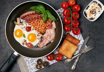 English breakfast. Fried eggs, sausages, bacon, beans, toasts, tomatoes on stone table. Top view with copy space
