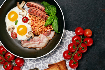 English breakfast. Fried eggs, sausages, bacon, beans, toasts, tomatoes on stone table. Top view with copy space