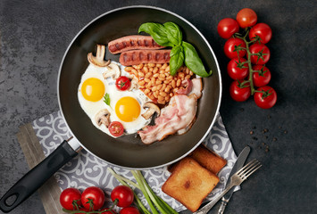 English breakfast. Fried eggs, sausages, bacon, beans, toasts, tomatoes on stone table. Top view with copy space