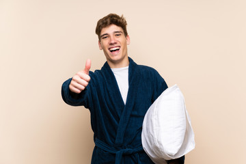 Handsome young man in pajamas over isolated wall with thumbs up because something good has happened