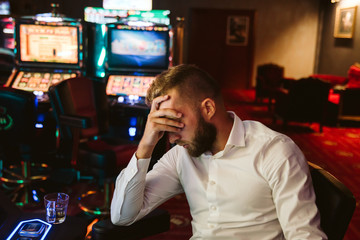 A man in a white shirt sits at a slot machine and loses his money