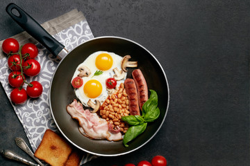 English breakfast. Fried eggs, sausages, bacon, beans, toasts, tomatoes on stone table. Top view with copy space