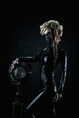 Young cyborg woman in leather suit and gas mask hand on a headlight