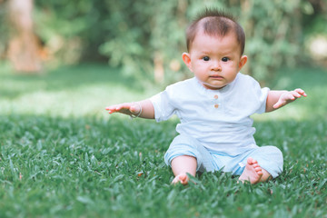 Asian male toddler sitting on grass in park. With copy space, curious look.