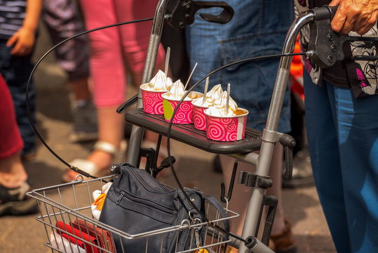 An old woman is driving on her wheeled walker yummy ice cream during a street party. Concept: food and drink