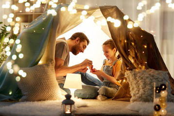 family, hygge and people concept - happy father and little daughter playing tea party in kids tent...