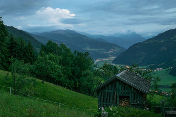 Fototapeta na wymiar Old hut in the mountains of the Alps with beautiful view over the valley at dusk. A thunderstorm rumbles in the distance.
