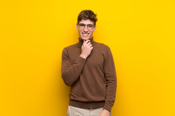 Handsome young man over isolated yellow background with glasses and smiling