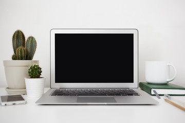 Fototapeta premium Modern technology, electronic devices, gadgets, job and occupation concept. White desk with cacti plants, mobile phone, diary and open laptop with empty black screen with copy space for your text