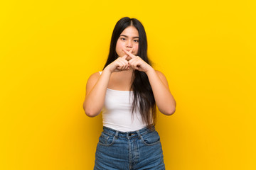 Young teenager Asian girl over isolated yellow background showing a sign of silence gesture