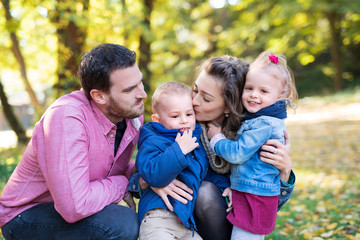 Fototapeta na wymiar Beautiful young family with small twins on a walk in autumn forest, kissing.