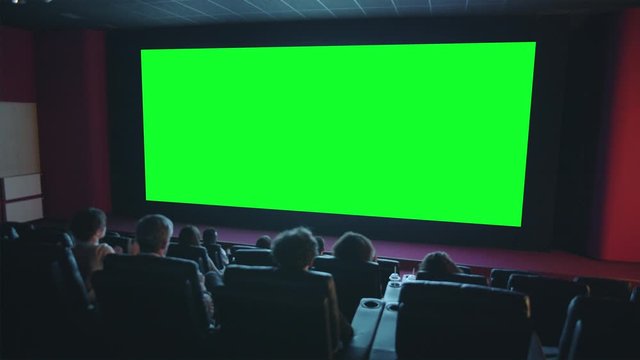 Slow motion of happy viewers crowd clapping hands looking at green chroma key cinema screen expressing admiration. Business, movie theater and emotions concept.