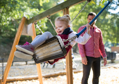 A Small Toddler Girl With A Father On A Swing On A