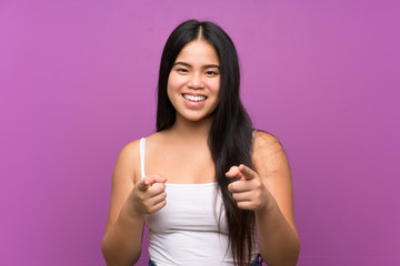 Young teenager Asian girl over isolated purple background points finger at you