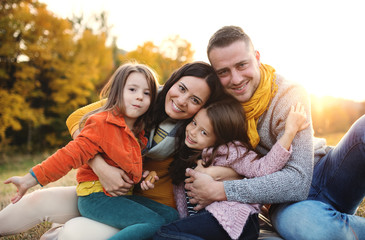 A portrait of young family with two small children in autumn nature at sunset.