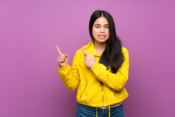 Young teenager Asian girl over isolated purple background frightened and pointing to the side
