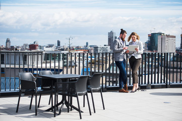 Two young business people with tablet standing on a terrace outside office, working.