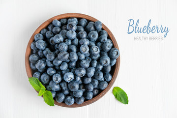 Closeup of blueberry berries with mint leaves in a clay plate on a light wooden background. Photo of blueberry for designers on the banner. Useful berries for sight