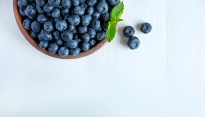 Closeup of blueberry berries with mint leaves in a clay plate on a light wooden background. Photo of blueberry for designers on the banner. Useful berries for sight
