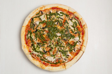 Italian pizza with chicken and mushrooms, on a white wooden table, poured with pesto