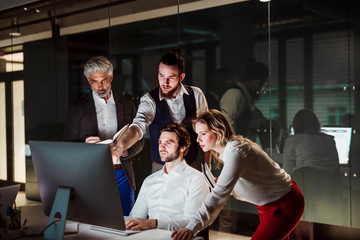 A group of business people in an office at night, using computer.