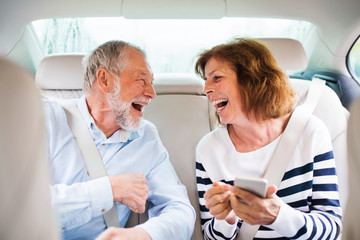 Cheerful senior couple sitting on back seats in car, laughing.