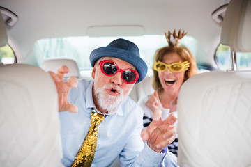 Cheerful senior couple with party accessories sitting in car, having fun.