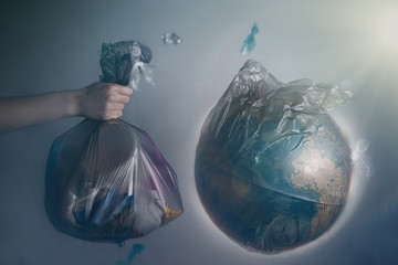 A woman's hand holds a garbage bag next to the globe of planet Earth. Concept of ecology and...