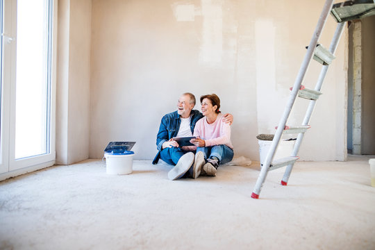 Senior couple painting walls in new home, using tablet. Relocation concept.