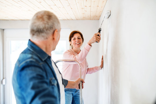 Senior couple painting walls in new home, relocation concept.