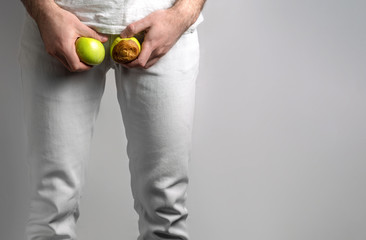 A man at the level of the genitals , holding a ripe and rotten apple. Disease for men. The concept...
