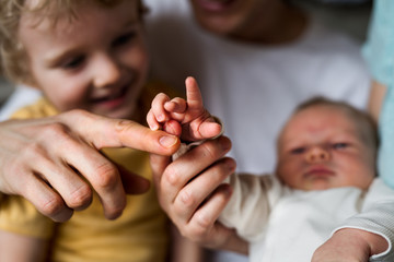 Midsection of father with newborn baby and small toddler son at home.