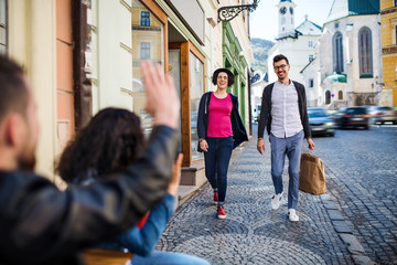 Young couple sitting in an outdoor cafe,greeting friends.