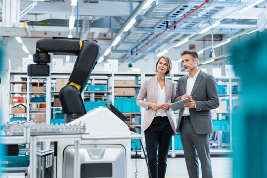 Businessman and businesswoman in a modern factory hall looking at robot