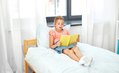 people, childhood and leisure concept - happy little girl reading book at home