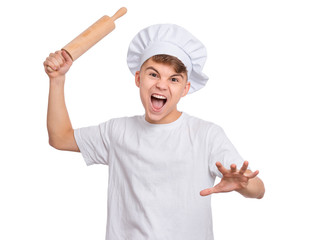 Mad teen boy in chef hat holding rolling pin, isolated on white background. Portrait of crazy screaming child with wooden rolling pin, shouting. Tools and equipment for cooking.