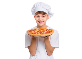 Happy handsome teen boy in chef hat holding cooked appetizing pizza. Guy holds plate with fresh pizza in his hands, isolated on white background. Portrait of cute child showing delicious Italian pizza